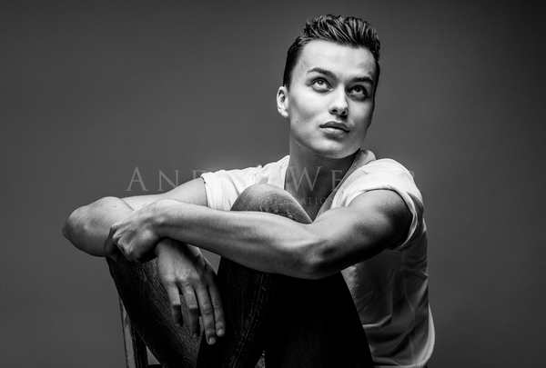 Junger Mann sitzend auf Stuhl fotografiert, hübsch muskulös weißes T-Shirt Blick nach oben Schwarzweiß Foto, Gay